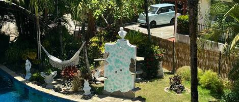 Zona de piscina con una hamaca, estatuas y un coche aparcado cerca.