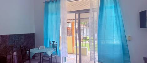 A room with a dining table and chairs, a sliding glass door leading to an outdoor area, and a TV mounted on the wall.