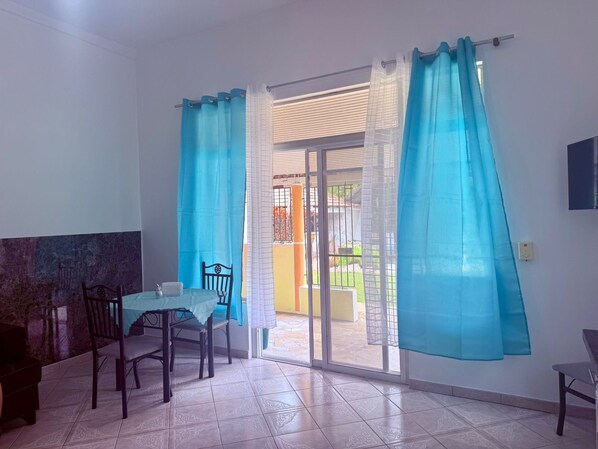 A room with a dining table and chairs, a sliding glass door leading to an outdoor area, and a TV mounted on the wall. - CasaLoca Cabarete (Cabarete)