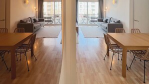 Een moderne woonkamer met een houten eettafel en stoelen, een bank en een balkon met uitzicht op gebouwen.