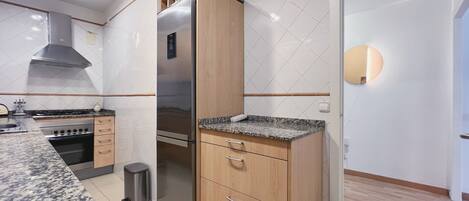A modern kitchen with a stainless steel refrigerator, wooden cabinets, granite countertops, a gas stove, and a built-in oven.