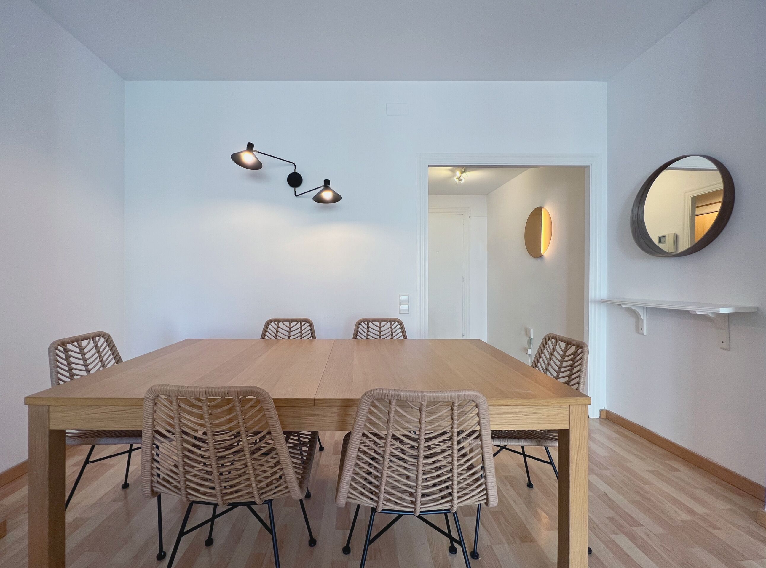 Un salón de conferencias con una larga mesa de madera, seis sillas de mimbre y tres lámparas colgantes.