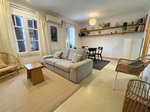 A living room with a sofa, a coffee table, wicker chairs, a dining table with chairs, a bookshelf, and a hanging light fixture. - Stay U-nique Apartments Borbó (Barcelona)