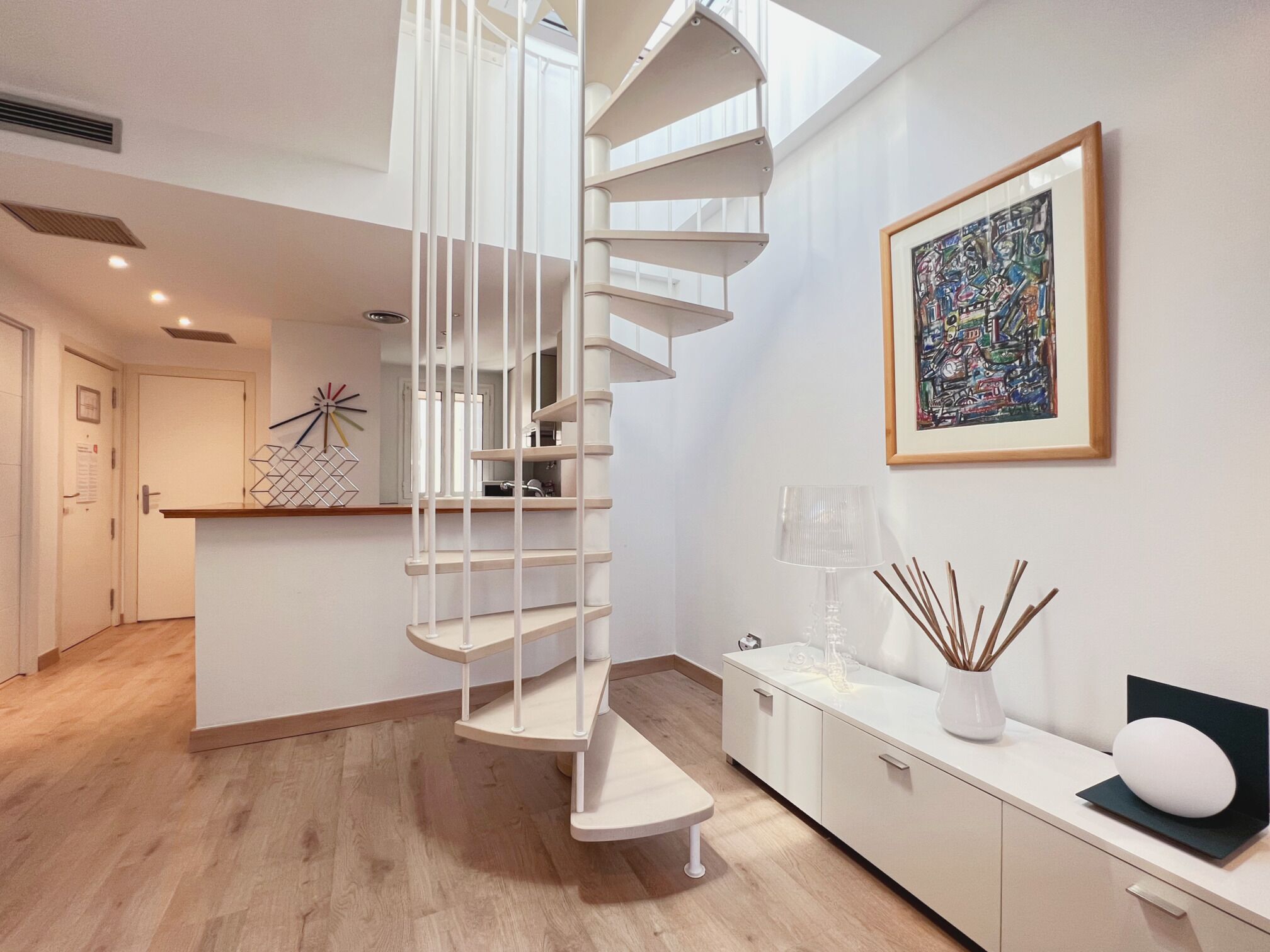 Un interior moderno con una escalera de caracol, una cocina minimalista y una obra de arte contemporánea en la pared.
