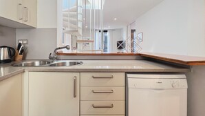 A modern kitchen with a dishwasher, stainless steel sink, and a wooden countertop.