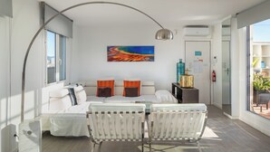 Une chambre d’hôtel moderne, équipée d’un lit, d’un coin salon avec deux fauteuils, d’une grande fenêtre et d’un tableau au mur.
