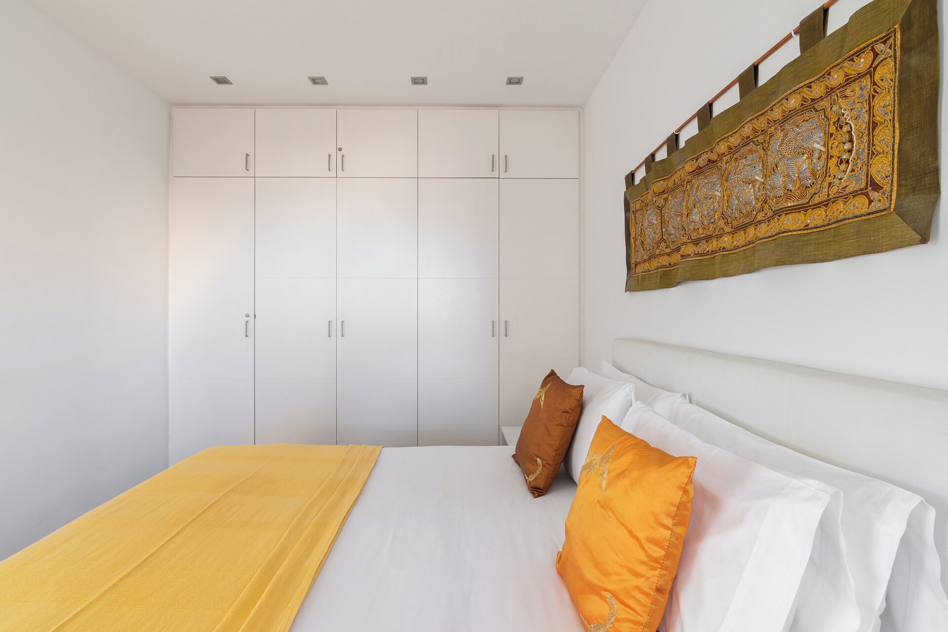 A bedroom with a bed, white wardrobe, and a decorative wall hanging.