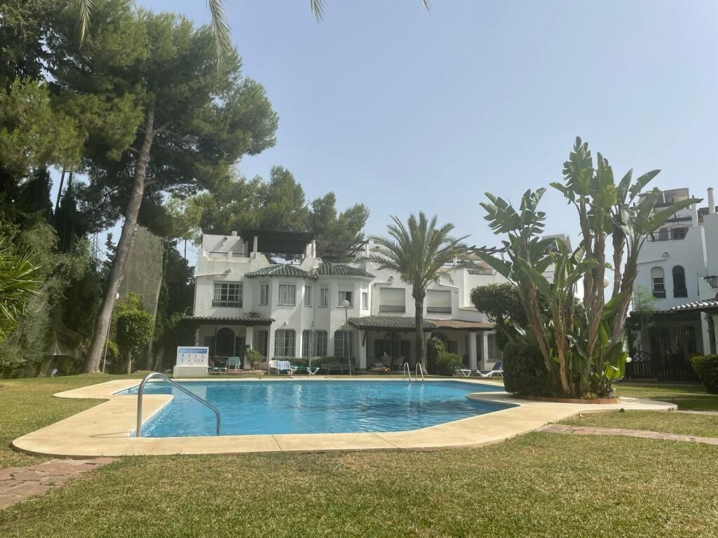 Une piscine entourée d’une pelouse, de palmiers, et un bâtiment avec de nombreuses fenêtres et des balcons en arrière-plan.