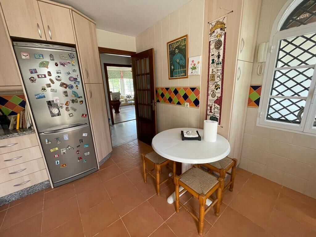 A kitchen with a refrigerator covered in magnets, a round dining table with chairs, and a window with a decorative grille.