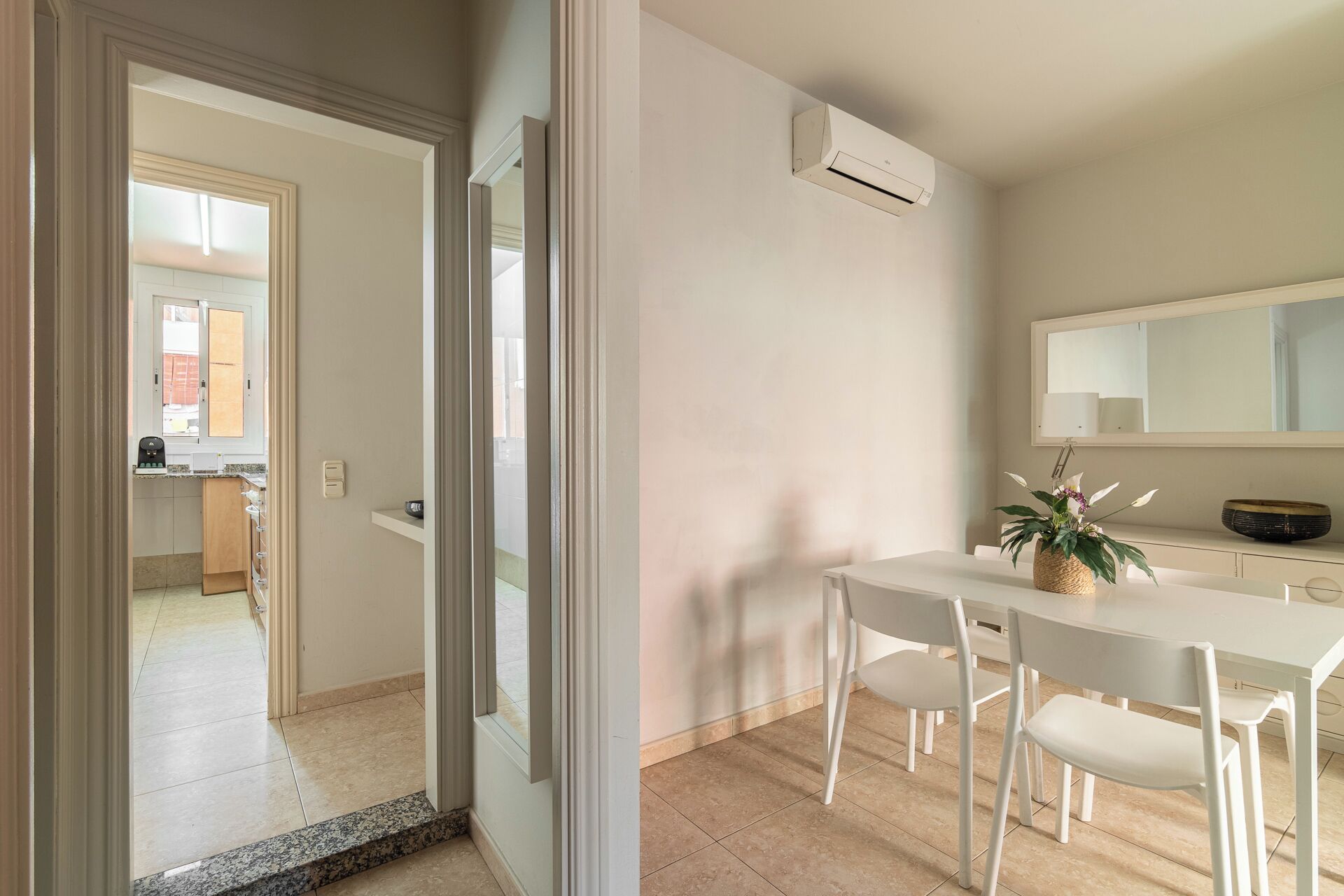 Een moderne keuken met een ingebouwde oven, een eethoek met een witte tafel en stoelen, en een grote spiegel boven de wastafel.