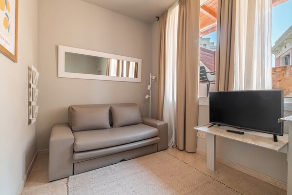 Ein modernes Wohnzimmer mit einer Couch, einem Flachbildfernseher auf einem Schrank, einem Spiegel an der Wand und einem Fenster mit Vorhängen.