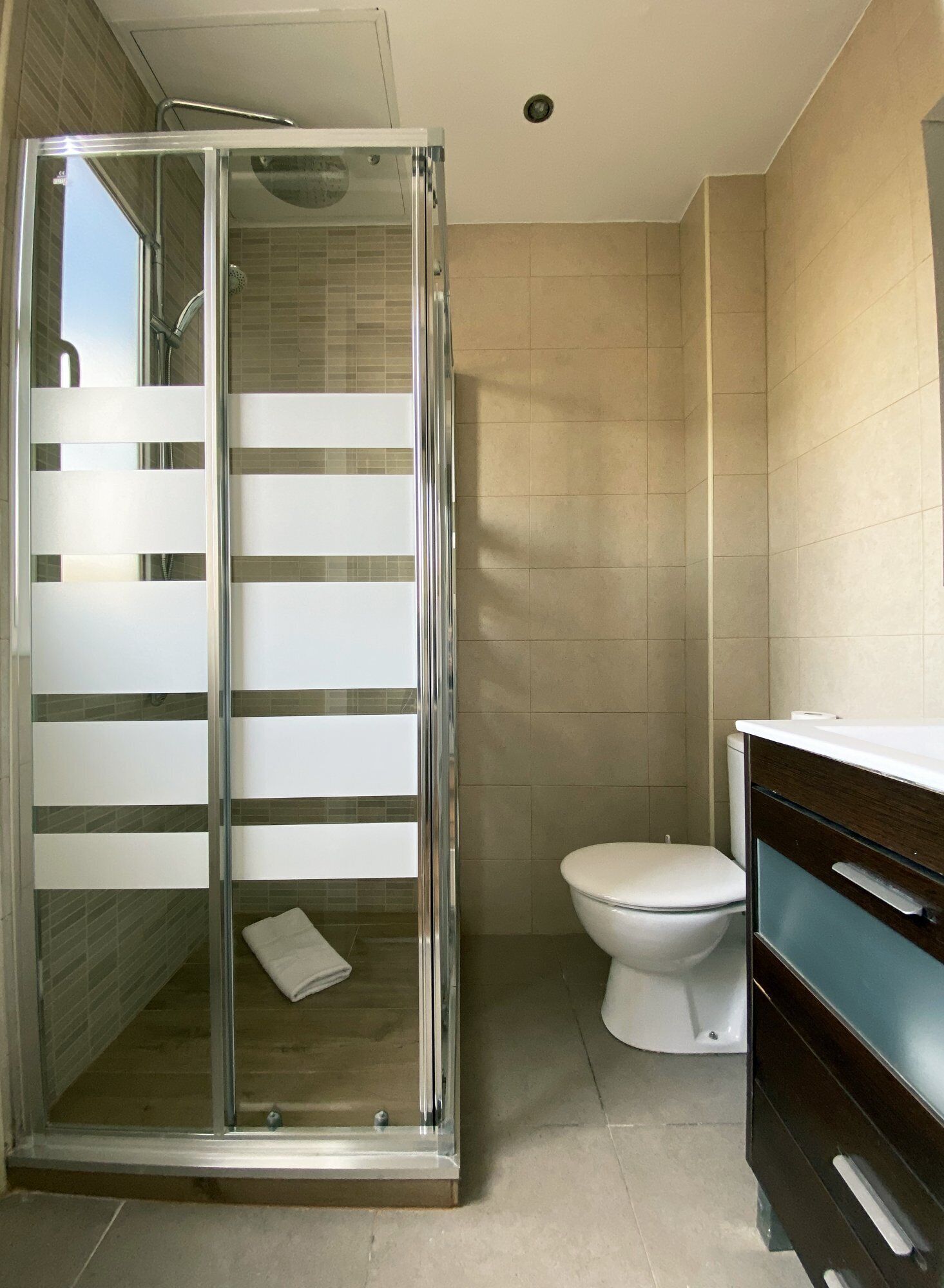 A bathroom with a glass-enclosed shower, a toilet, and a vanity with drawers.