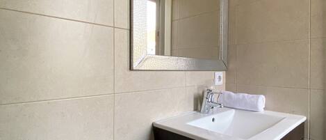 Une salle de bain moderne avec des toilettes blanches, un lavabo blanc et un meuble sombre en dessous, ainsi qu’un miroir au-dessus du lavabo.