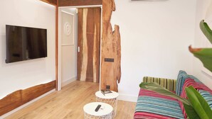 A modern living room with a wooden accent wall, a flat-screen TV mounted on the wall, a small round table with a remote control, and a colorful striped sofa. - Stay U-nique Apartment Padilla (Barcelona)