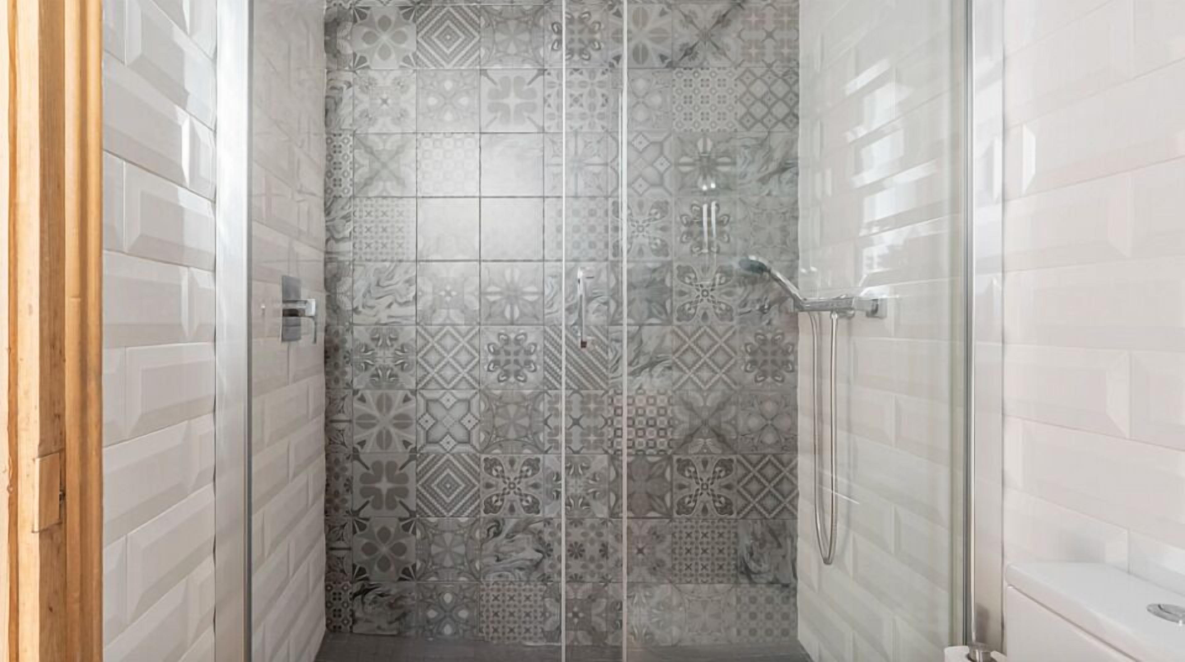 Une douche avec des carreaux décorés et une porte en verre.