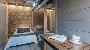 Ein Schlafzimmer mit einer Steinswand, einem Bett mit weißer Bettdecke, einem Holfnachtkästchen mit Buch und Tasse sowie einer Schiebetür.
