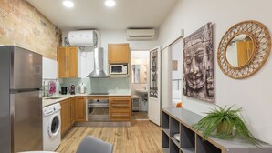A modern kitchen with wooden cabinets, a stainless steel refrigerator, a built-in oven, and a microwave. There is a washing machine, a sink, and a coffee maker. The room has a brick wall, a ceiling fan, and a large mirror. - Stay U-nique Apartments Caminal (Barcelona)