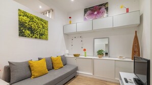 A modern living room with a grey sofa, yellow cushions, a flat-screen TV, and a wooden floor. - Stay U-nique Apartments Caminal (Barcelona)