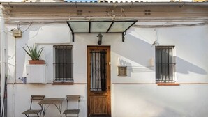 A white building with a wooden door, two windows with metal bars, a small table with chairs, and a potted plant. - Stay U-nique Apartments Caminal (Barcelona)