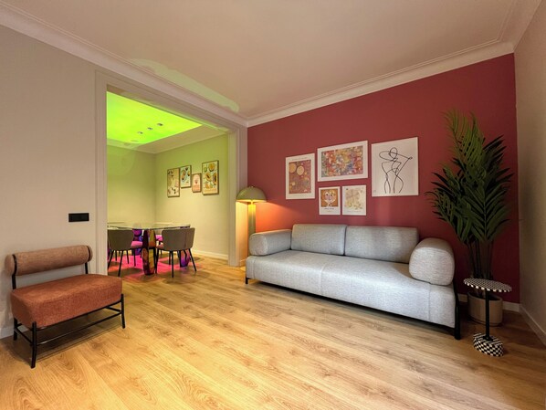 A living room with a grey sofa, a bench, a dining area with chairs, and a table.