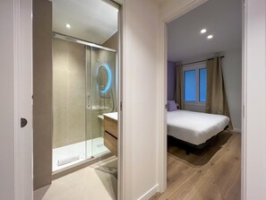 Ein modernes Hotelzimmer mit einer gläsernen Duschkabine, einem Nachttisch, einem Bett und einem Fenster mit Vorhängen.