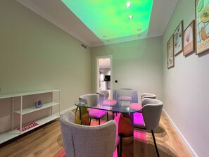 A modern dining area with a glass table, grey upholstered chairs, and a pink accent chair.