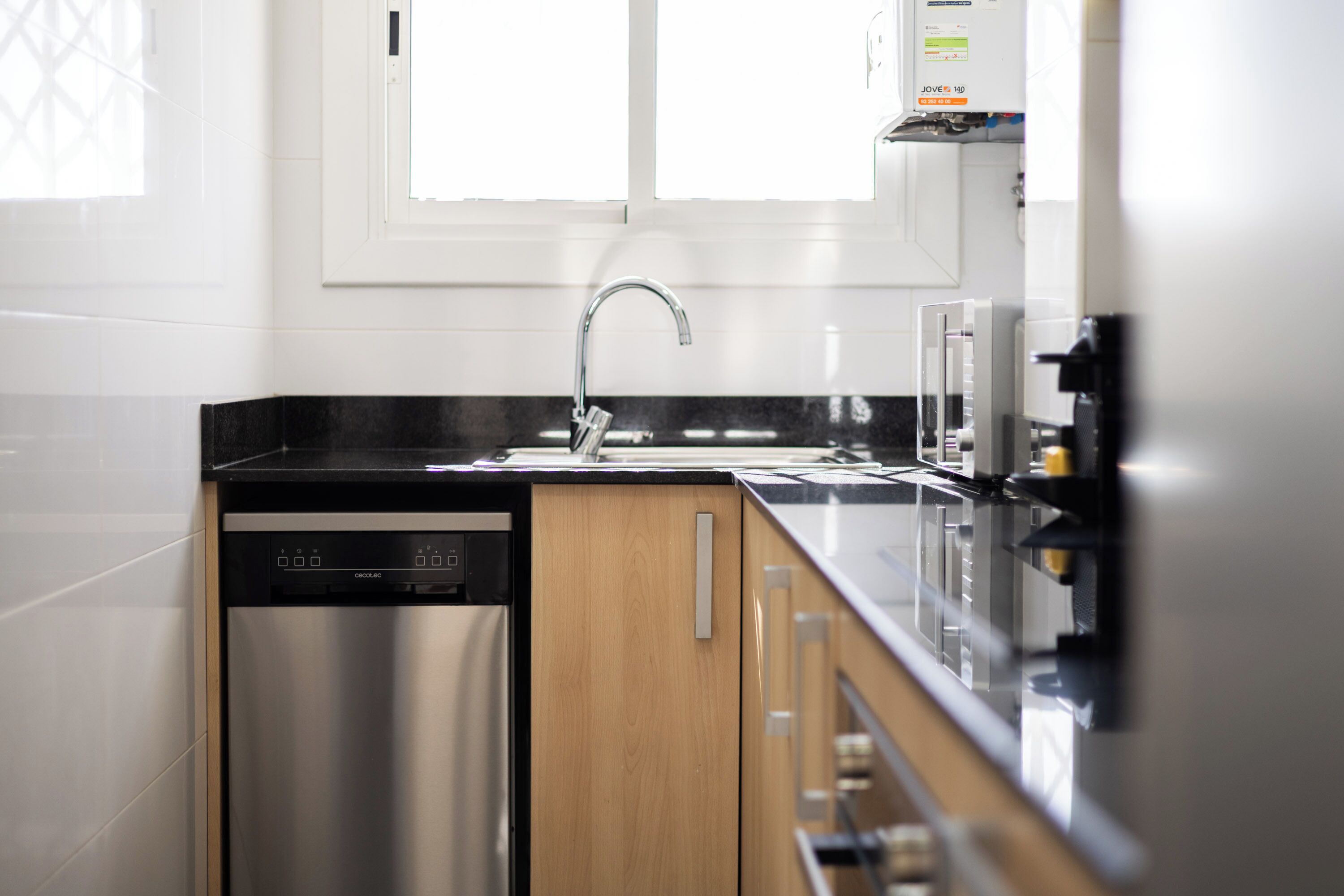 Una cucina moderna con lavastoviglie, lavello in acciaio inox e mobili in legno.