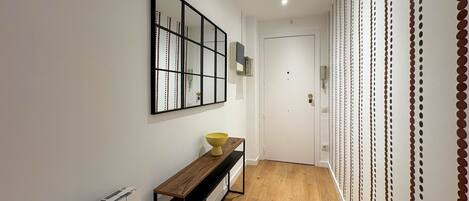 Un pasillo con suelo de madera, un banco, un espejo en la pared y una puerta.
