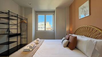 Habitación de hotel con cama, ventana con vista a la ciudad, estantería de metal negro y un cuadro en la pared.