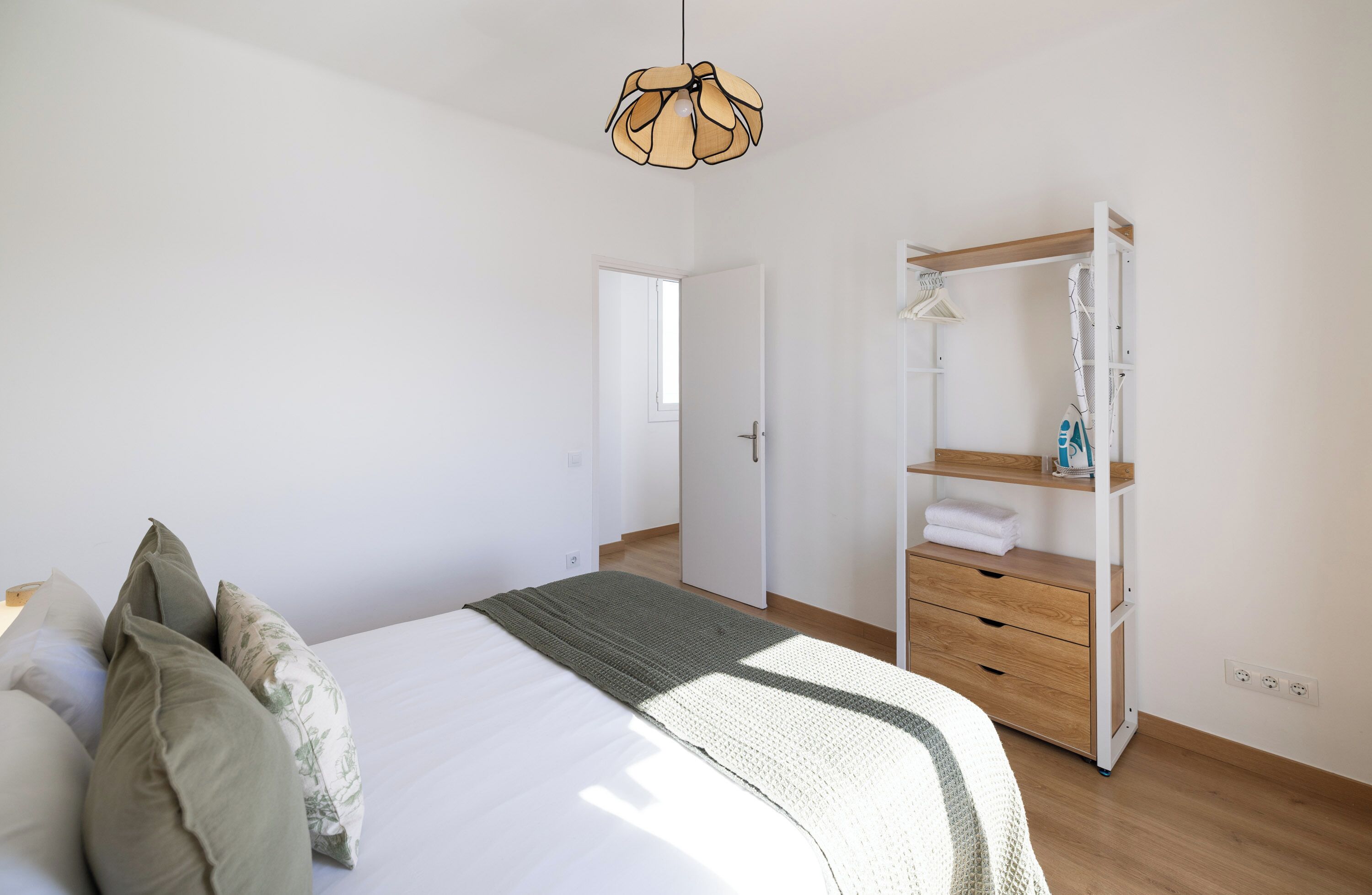 A bedroom with a bed, a wardrobe, a hanging light fixture, and a door leading to another room.