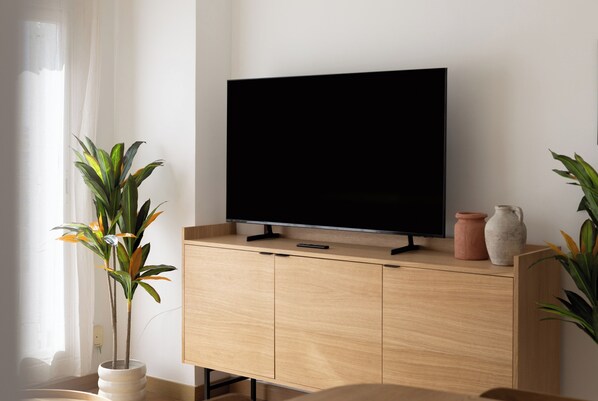 A modern living room with a flat-screen TV on a wooden cabinet, a potted plant, and a vase. - Stay U-nique Apartment Corsega II (Barcelona)