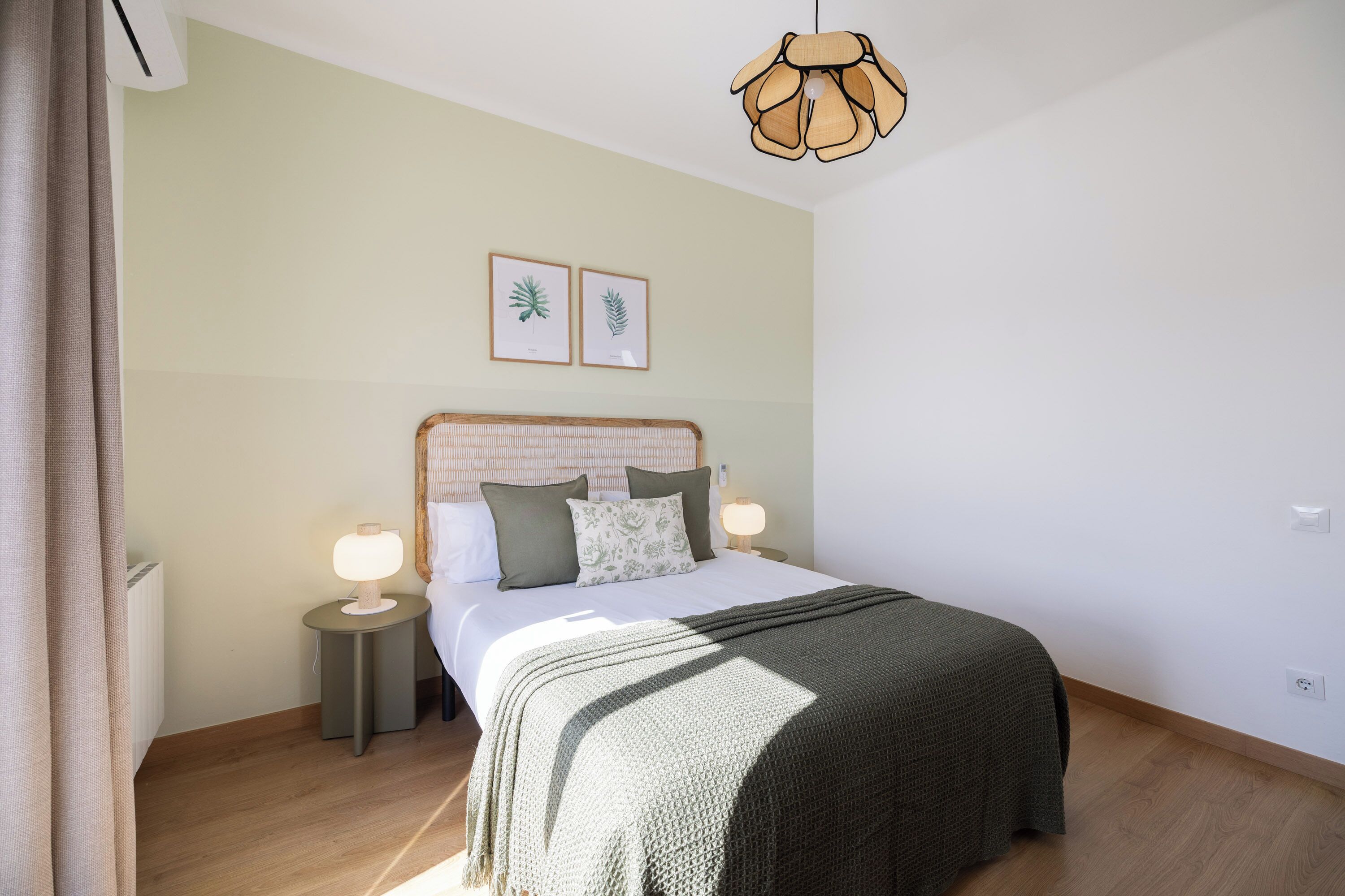 Een slaapkamer met een bed, bedlampen, een hanglamp en ingelijste plantendrukken aan de wand.