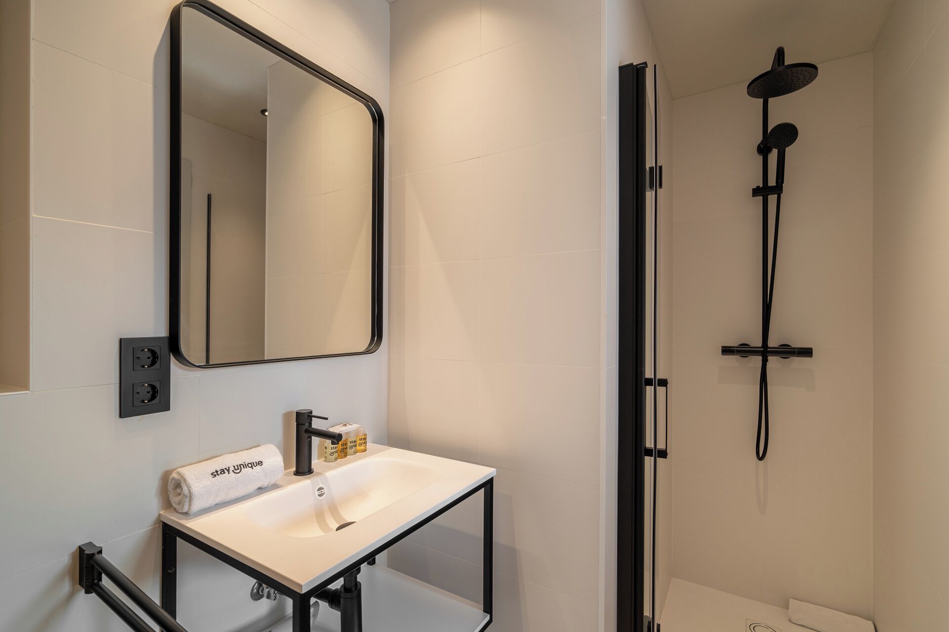 Un baño moderno con lavamanos blanco, espejo y ducha con marco negro.