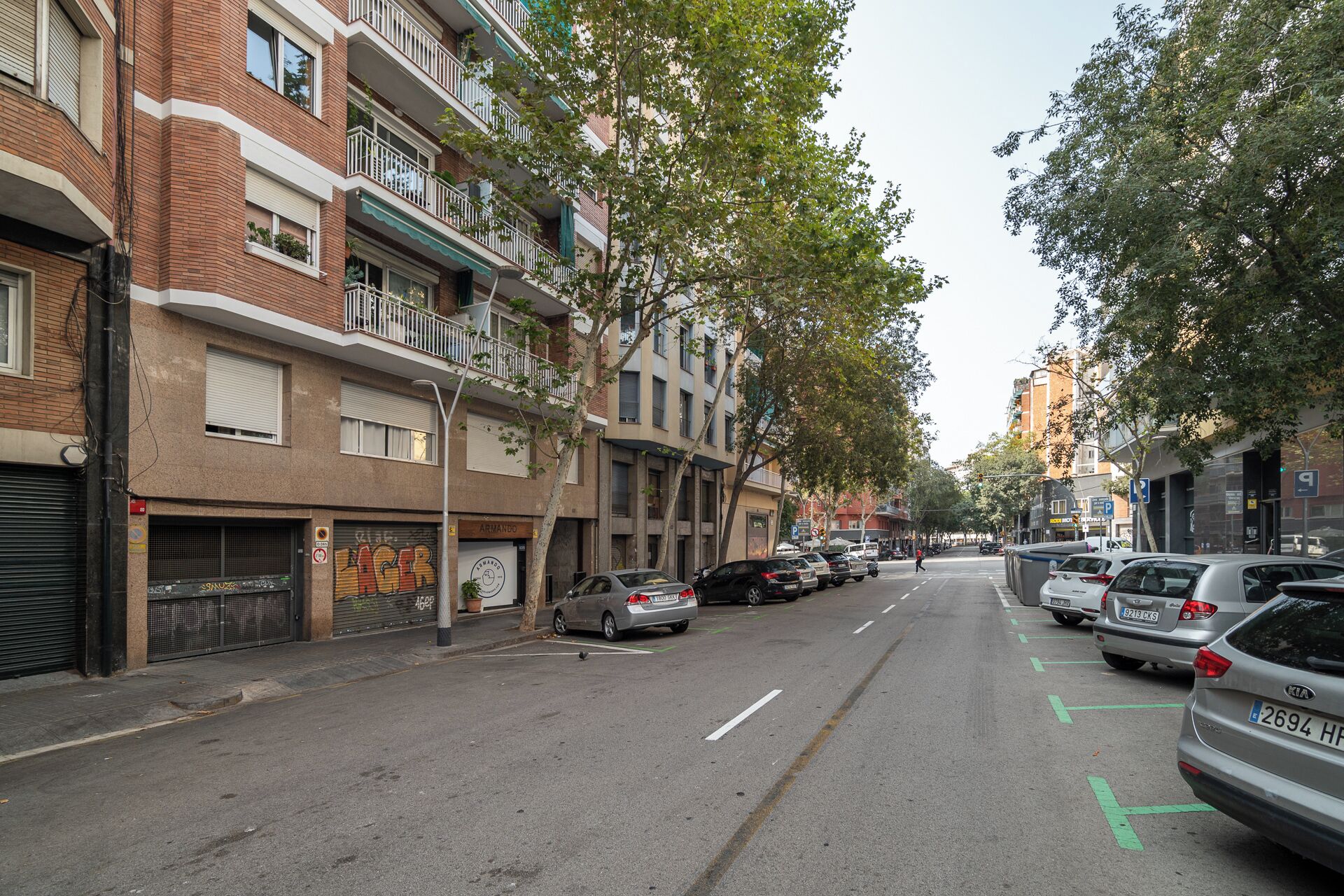 Un edificio residencial de varios pisos con balcones, autos estacionados y una calle despejada.