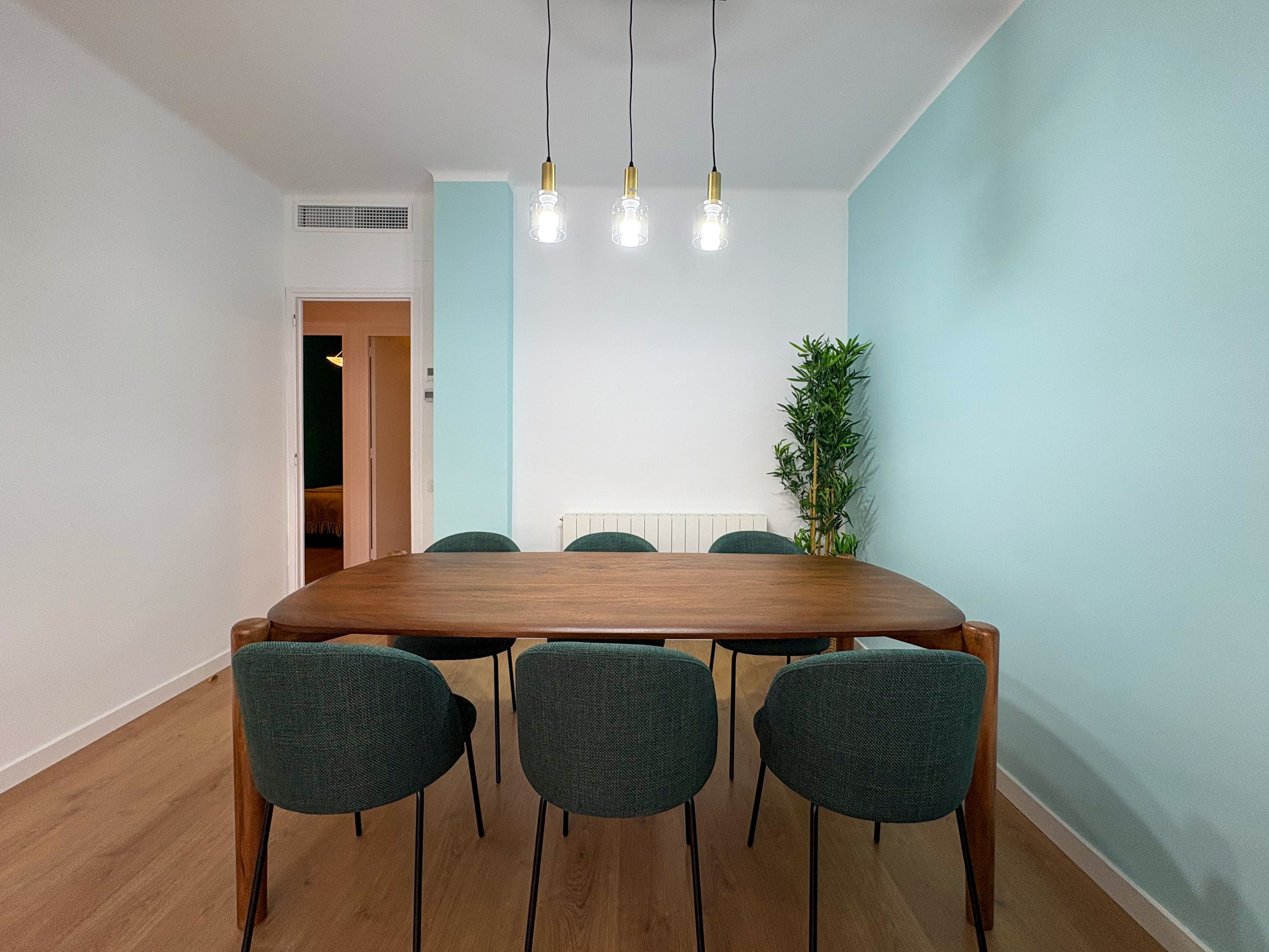Uma sala de jantar com mesa de madeira, quatro cadeiras e uma planta.