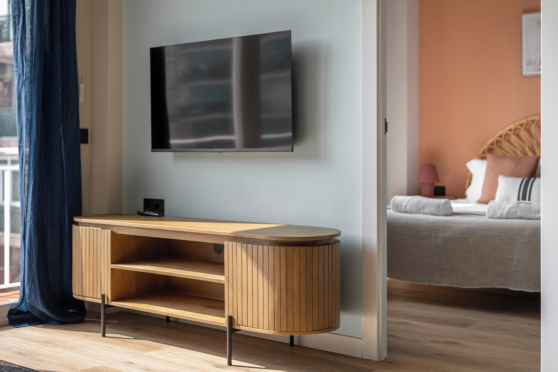 Een moderne hotelkamer met een houten console tafel, een flatscreen televisie aan de muur en een bed met hoofdbord en kussens.