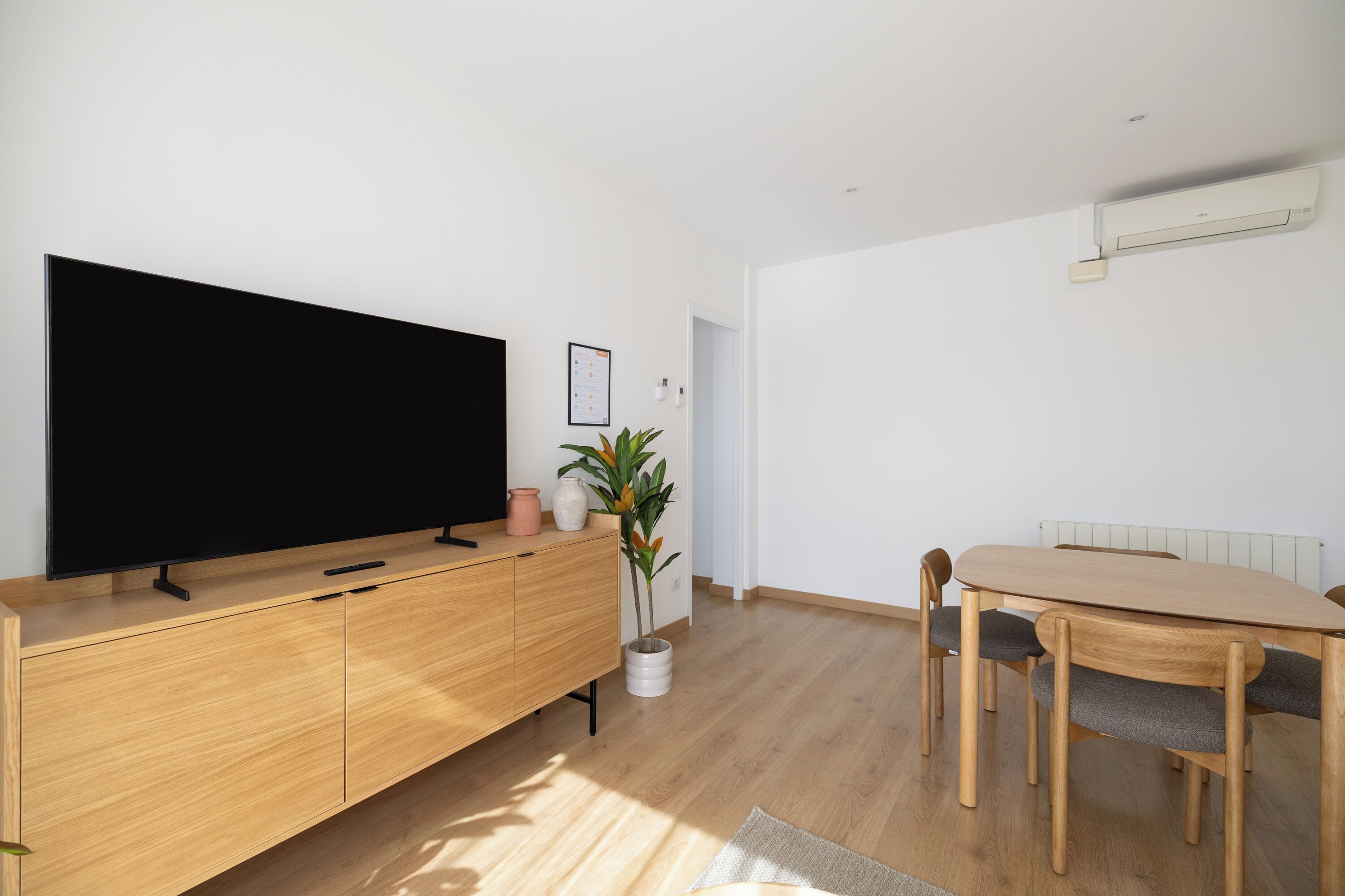A modern living room with a flat-screen TV, wooden furniture, a dining table, and a radiator.
