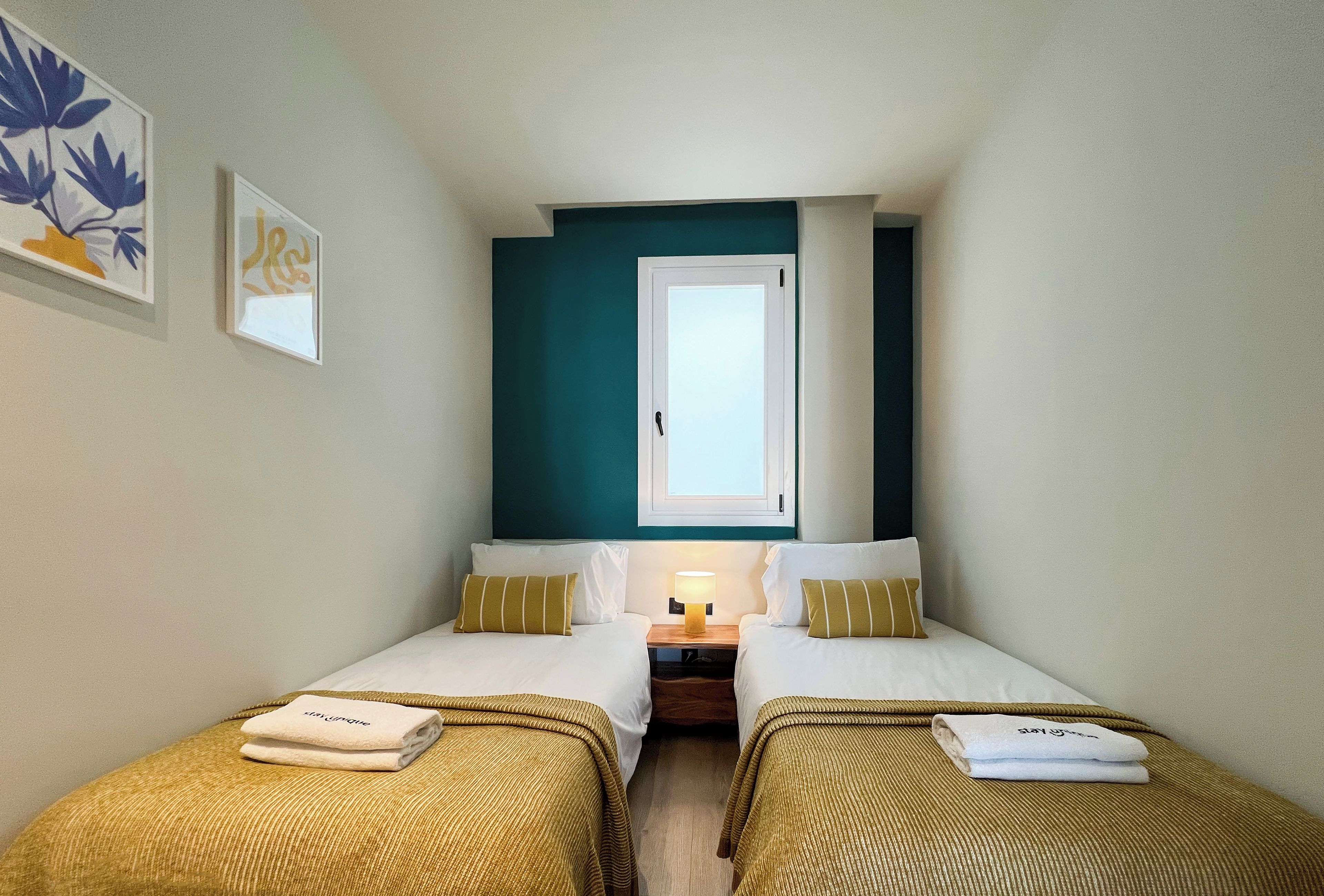 A small, cozy room with two beds, a nightstand, and a window.