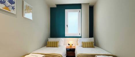 A small, cozy room with two beds, a nightstand, and a window.
