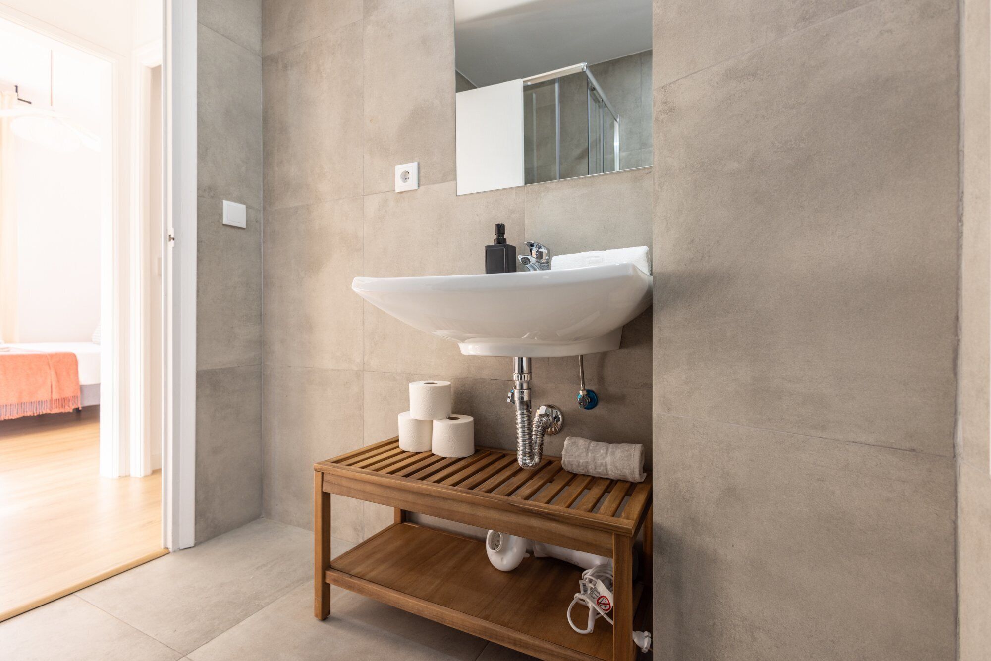 A bathroom with a white sink, a wooden shelf, and a towel rack.