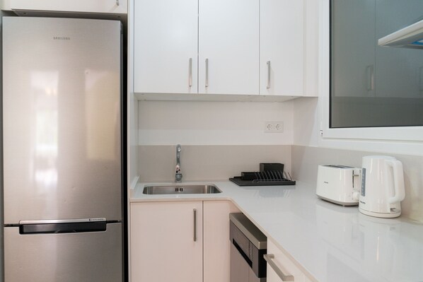 A modern kitchen with a stainless steel refrigerator, white cabinets, a sink, a toaster, and a coffee maker.