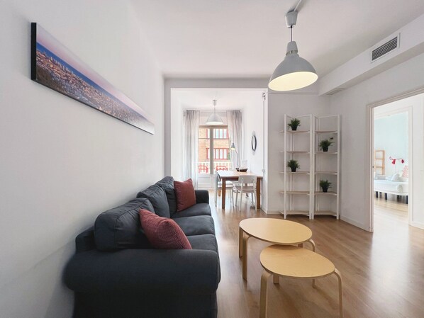 Un salon moderne comprenant un canapé, deux petites tables, un coin repas et une étagère blanche.
