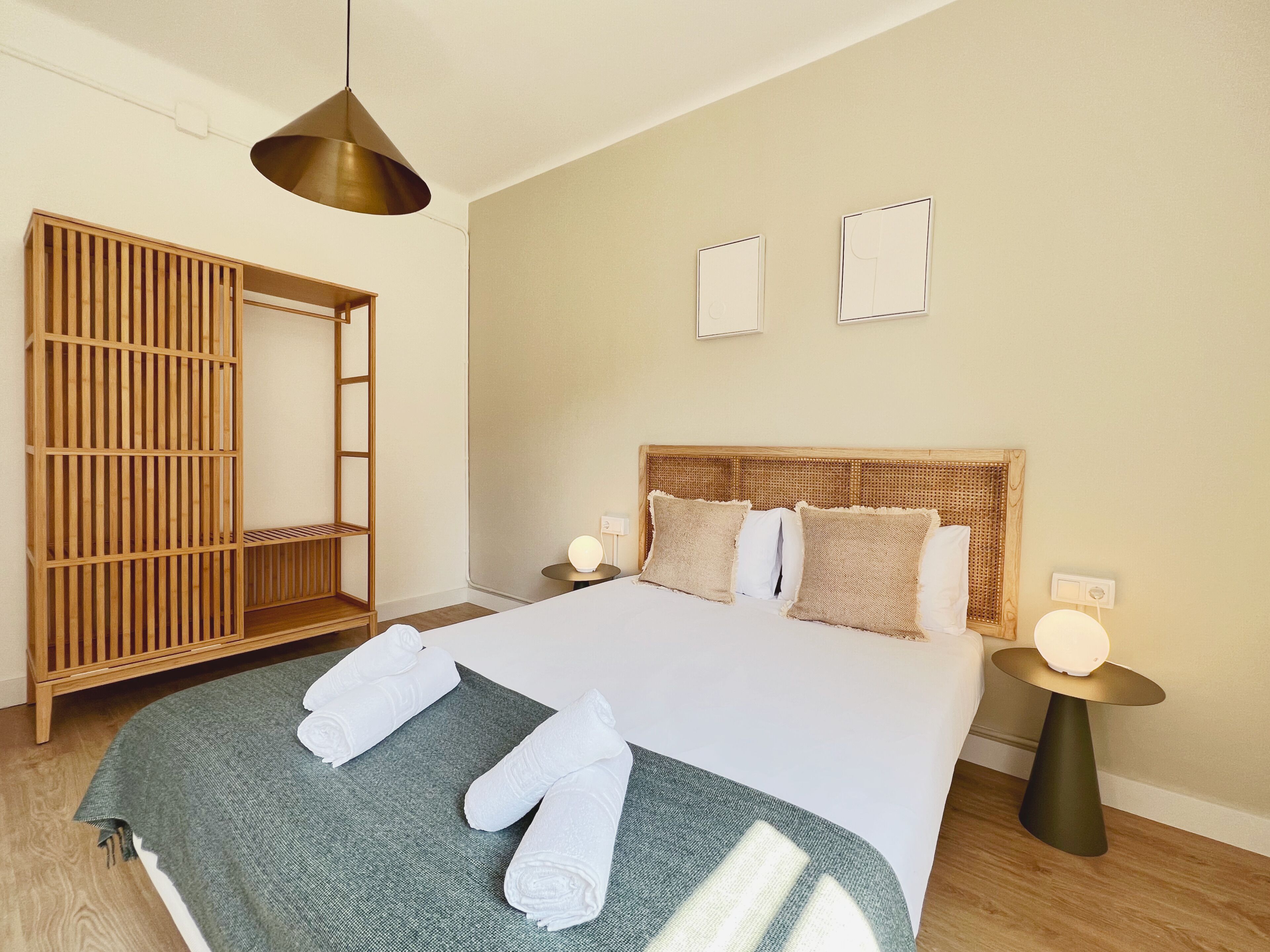 Un dormitorio con cama, lámparas de noche, un armario de madera y una mesa redonda.