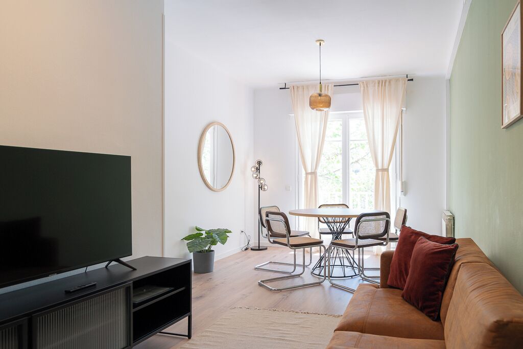 Ein modernes Wohnzimmer mit Flachbildfernseher, einer Couch, einem Esstisch mit Stühlen und einer Topfpflanze.