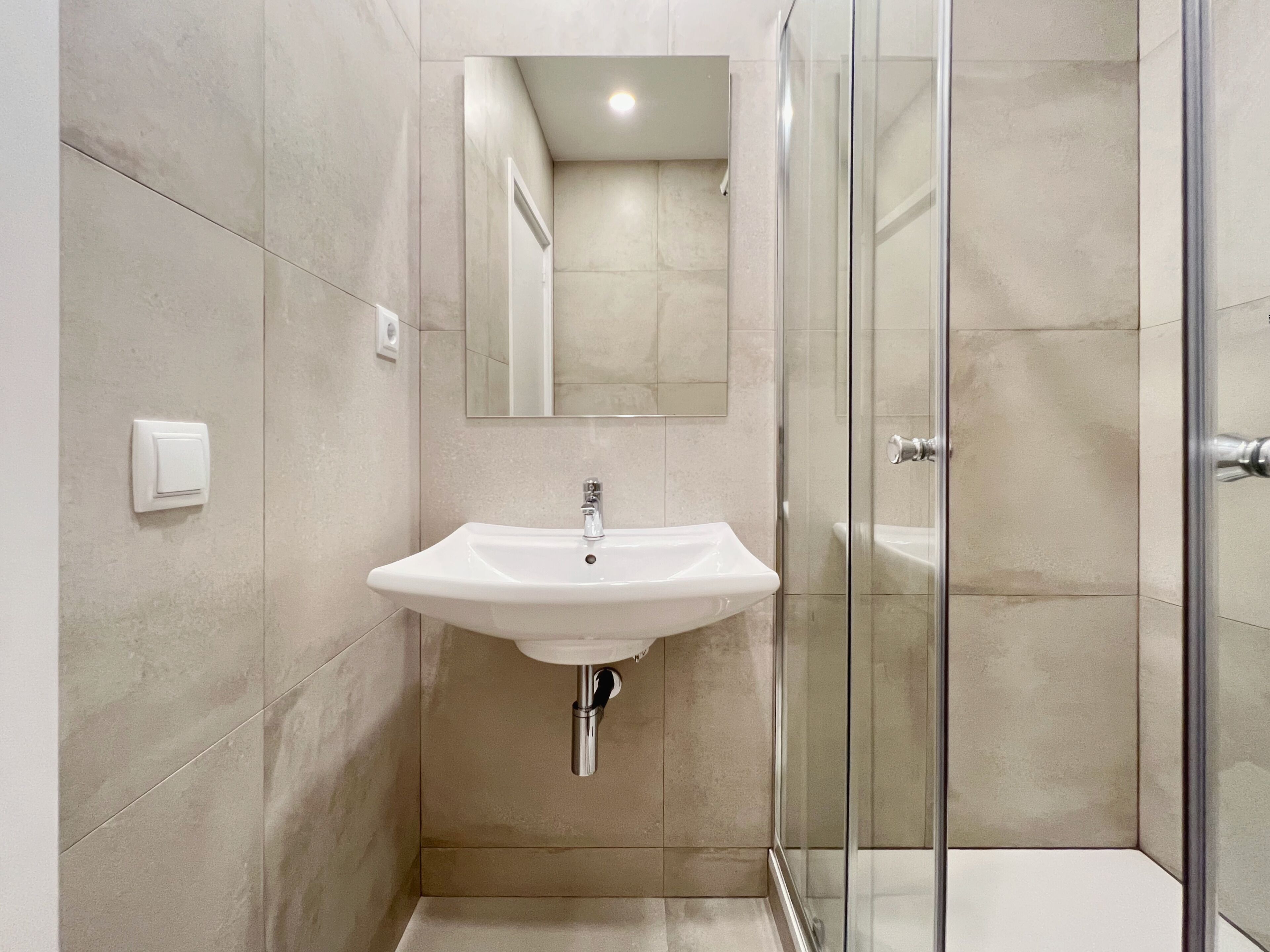 A modern bathroom with a white sink, a mirror, and a glass shower enclosure.