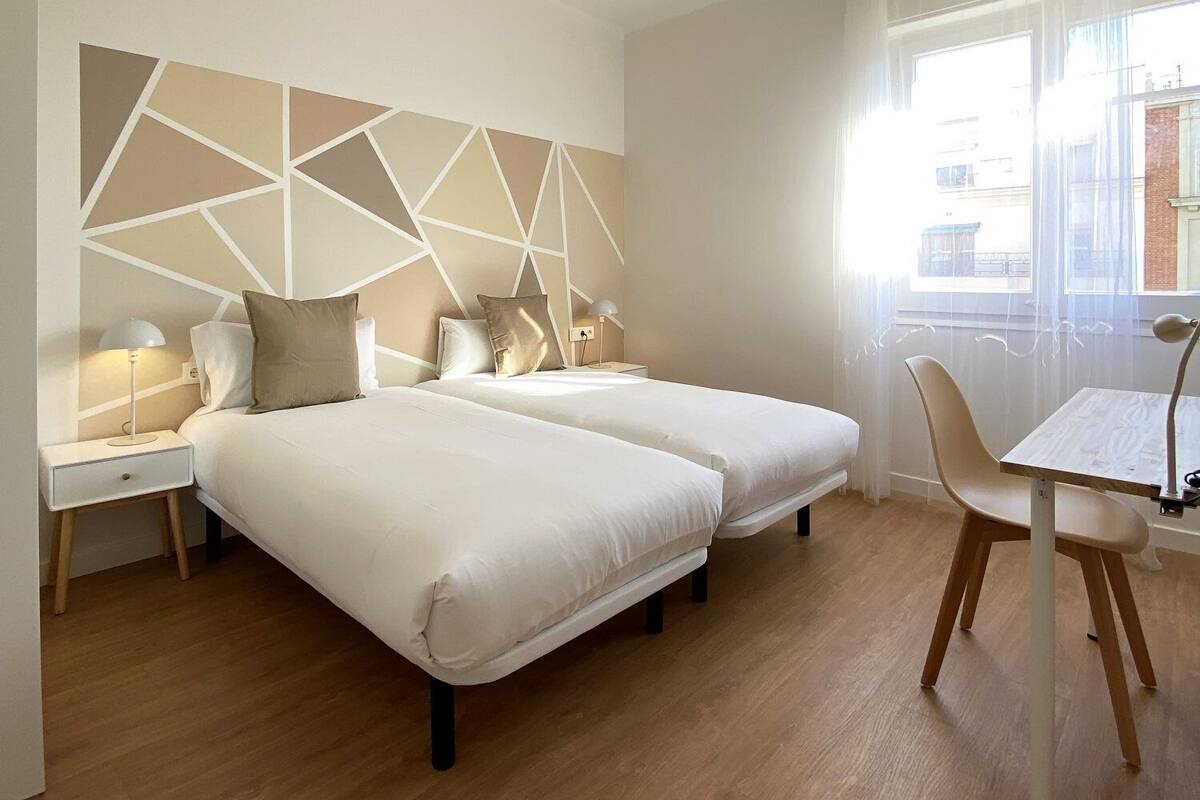 Une chambre d’hôtel avec deux lits, un bureau, une chaise et une fenêtre avec des rideaux.
