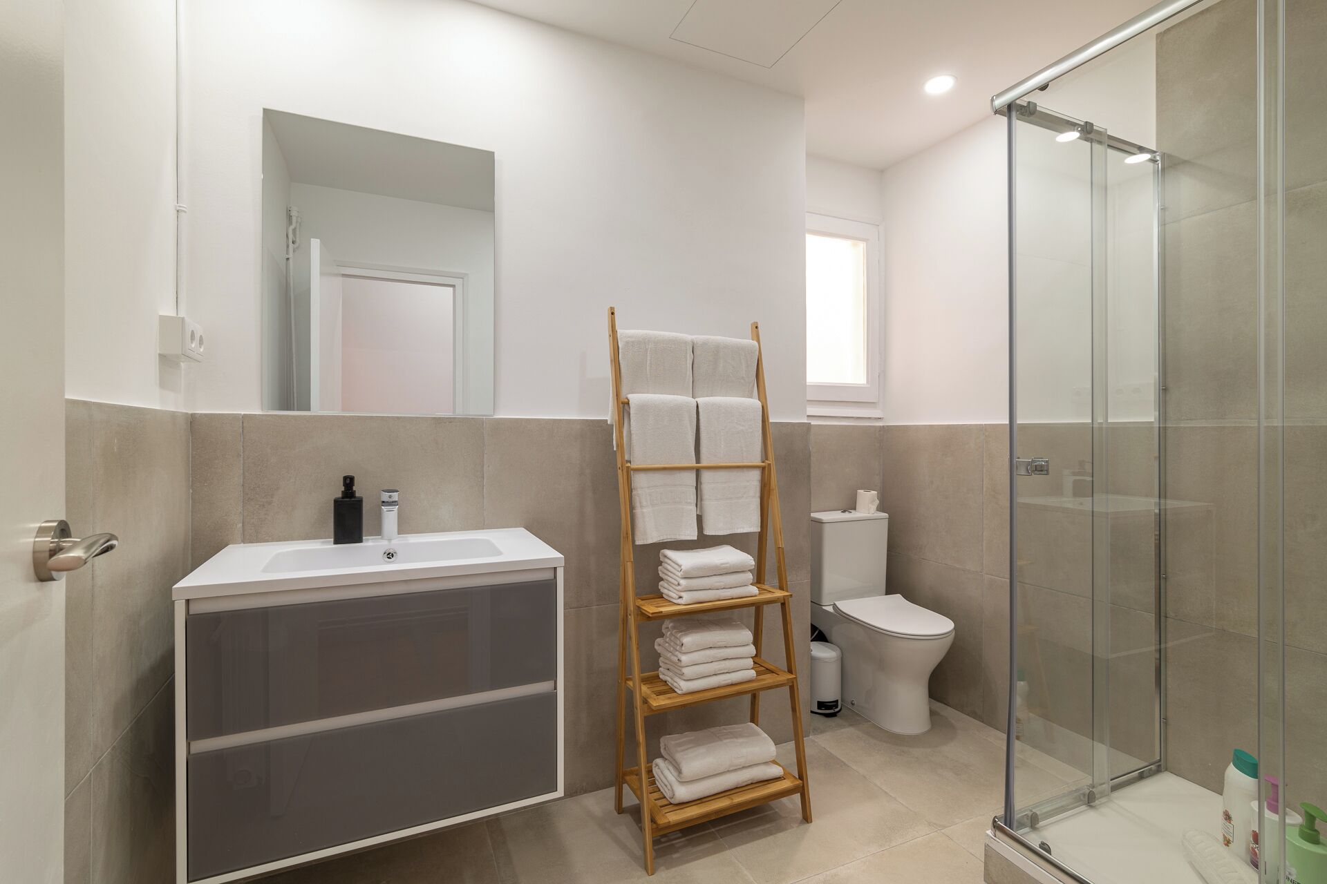 A modern bathroom with a glass shower enclosure, a wooden towel rack, and a white sink.