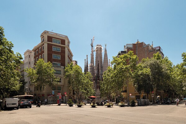 A city street with modern buildings, a prominent cathedral, and a central square with potted plants.