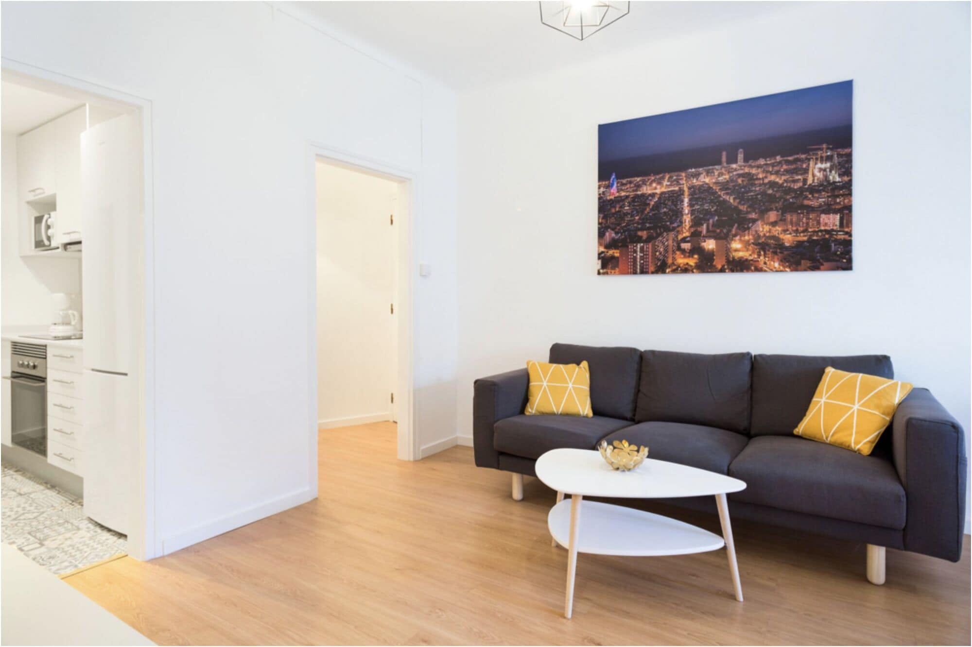 Un salon moderne avec un canapé foncé, une table basse blanche et un tableau représentant un paysage urbain accroché au mur.