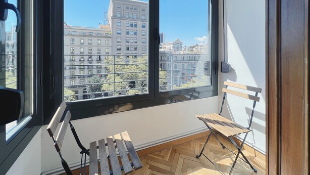 Ein Zimmer mit großem Fenster, einer hölzernen Bank und einem Fischgrätparkett.